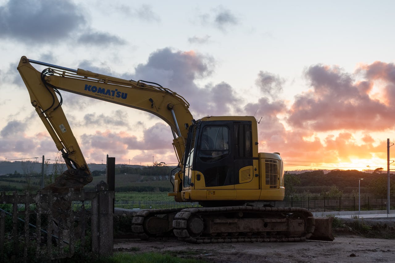 Silhouette of excavator working at sunset on a construction site with vibrant sky.